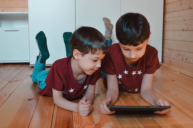 two boys lying on the floor looking at a tablet computer