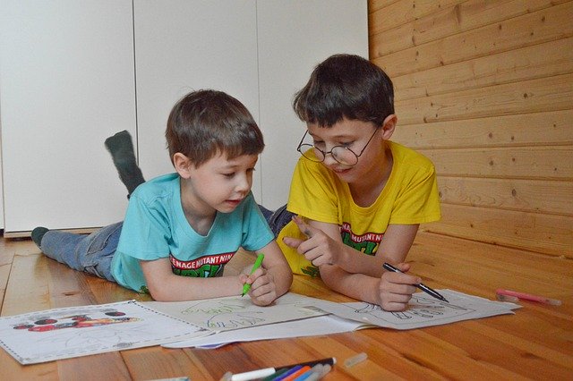 two boys coloring on paper while lying on the floor